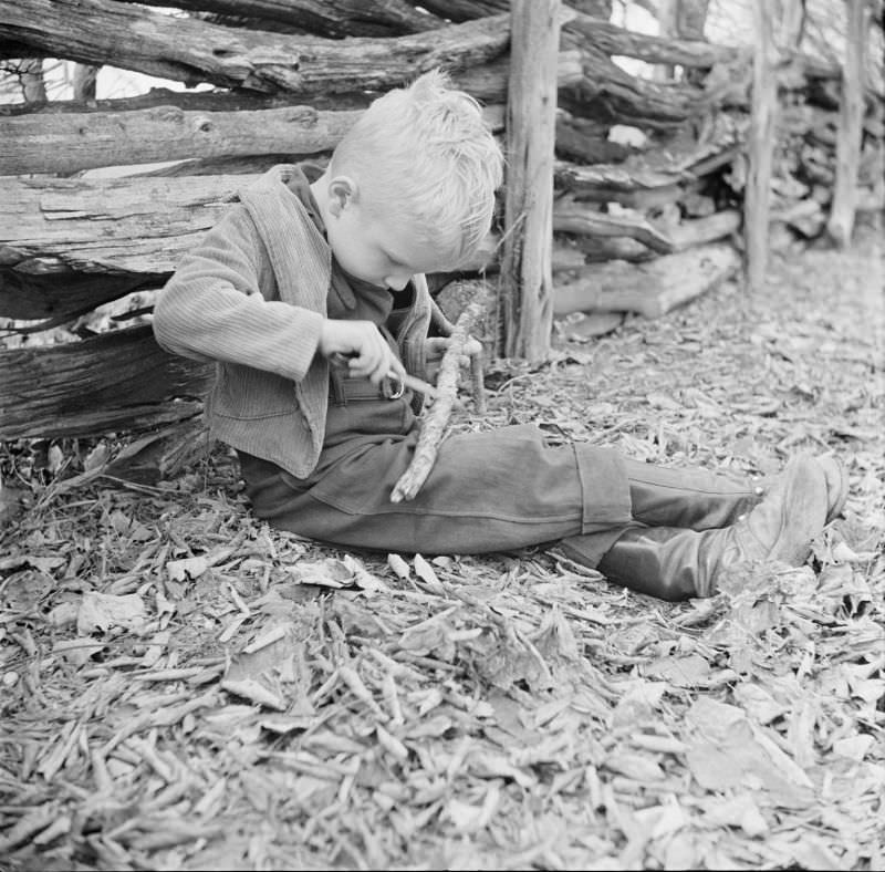 #13 Boy sitting on ground outside, holding two sticks