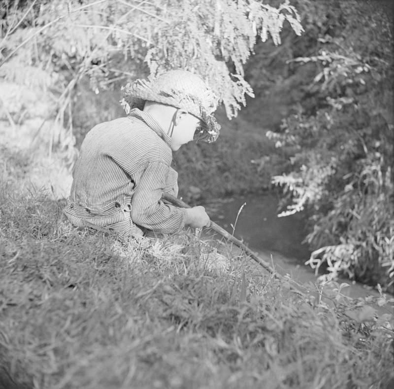 #19 Boy wearing a straw hat, sitting outside with a stick