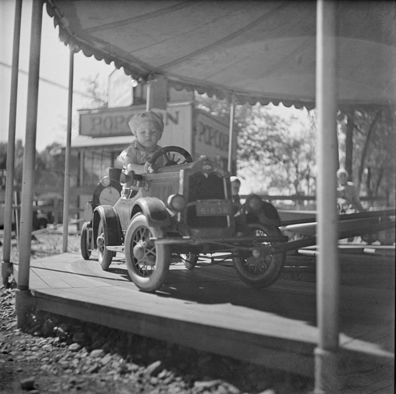 #28 Little boy sitting in toy car on carousel at amusement park