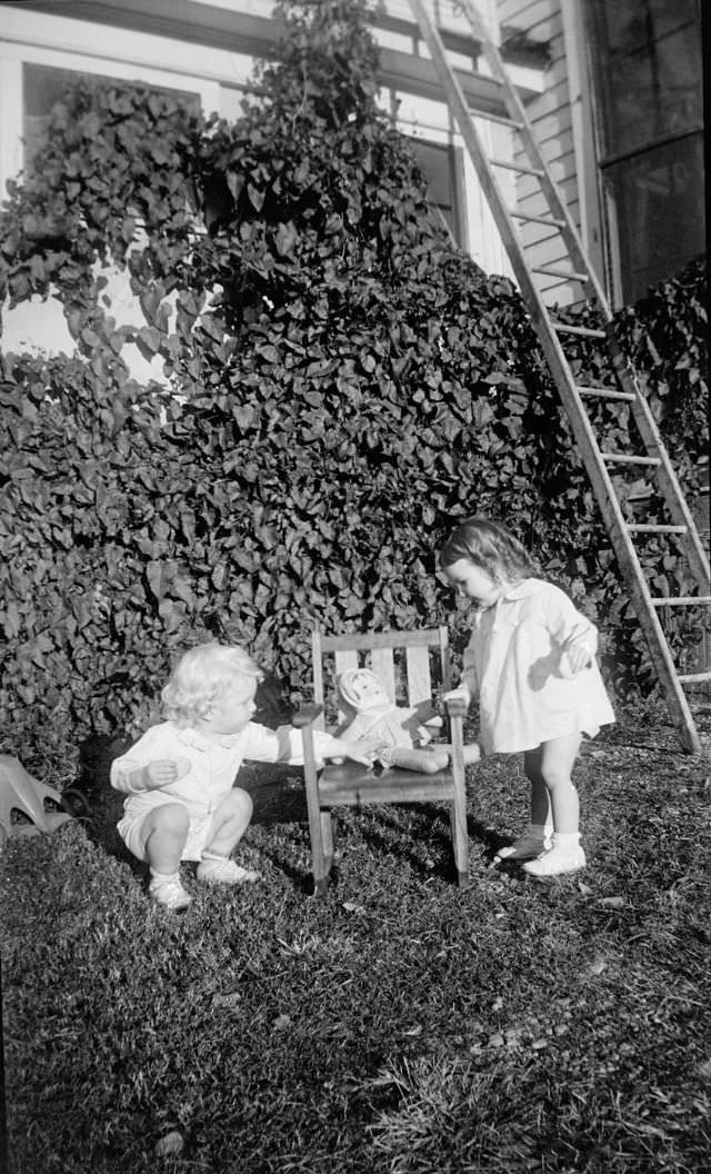 #40 Two little girls standing next to a child-size chair with a doll on it
