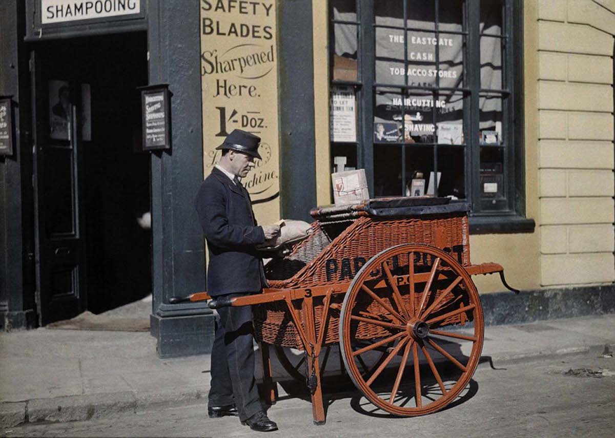 #23 A postman delivers packages with his parcel post barrow in front of a shop in Oxford offering ‘haircutting and shaving’ in 1928.