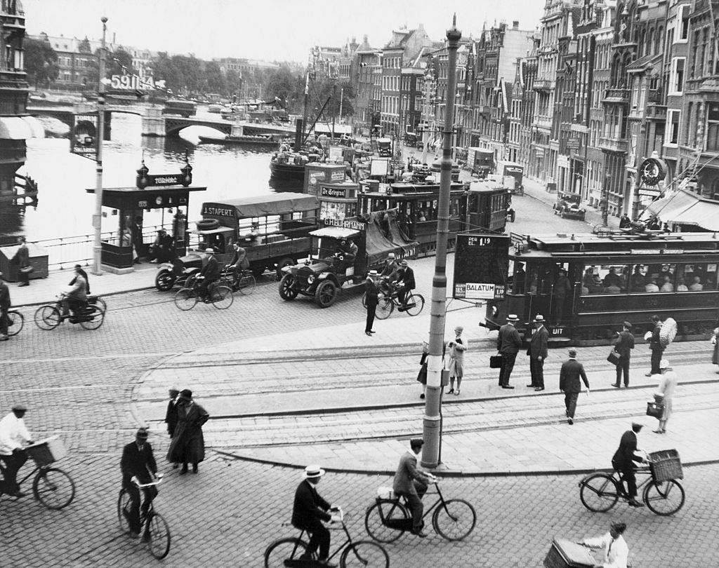 #5 Traffic scene on one of the principal streets of the Dutch capital. It includes bicycles, automobiles, trucks, trolleys, buses, pedestrians, and freight boats on the canal, 1950s.