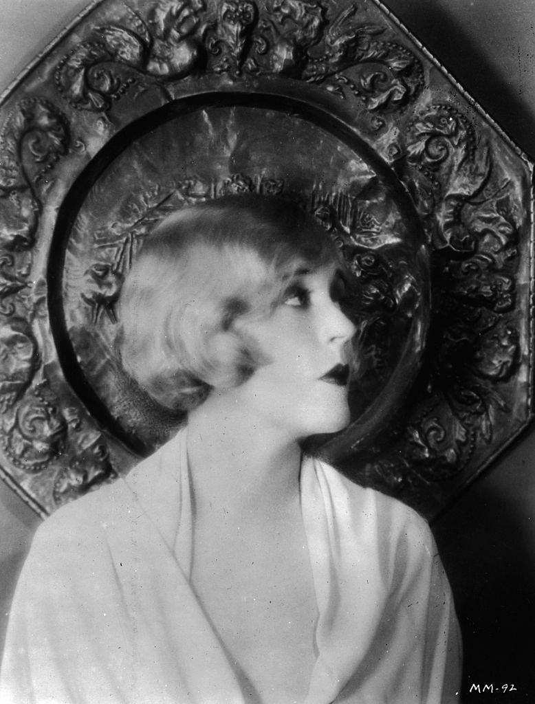 #25 Mae Murray poses in front of an ornamental plaque, 1925.