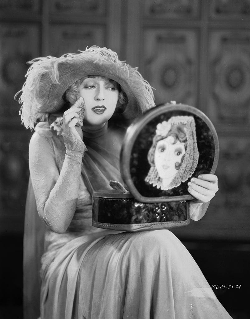 #46 Mae Murray making herself up in a mirror in the lid of her make-up box, 1926.