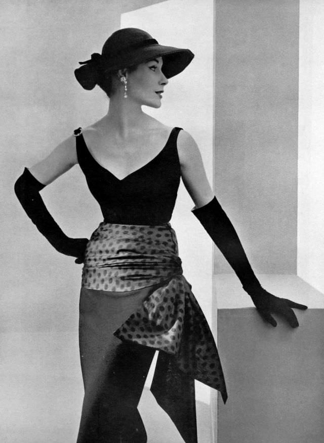 #3 Myrtle Crawford in black wool sheath, rhinestones adorn the straps and a draped blue silk polka dot highlights the hips, by Manguin, 1953