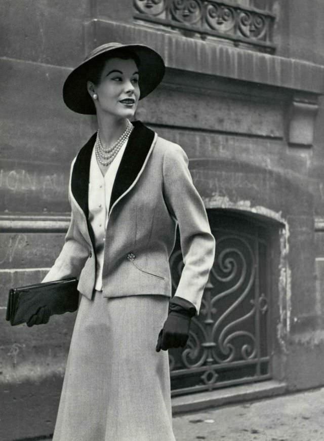 #19 Myrtle Crawford in gray wool suit with black velvet shawl collar worn over white piqué vest, 1953