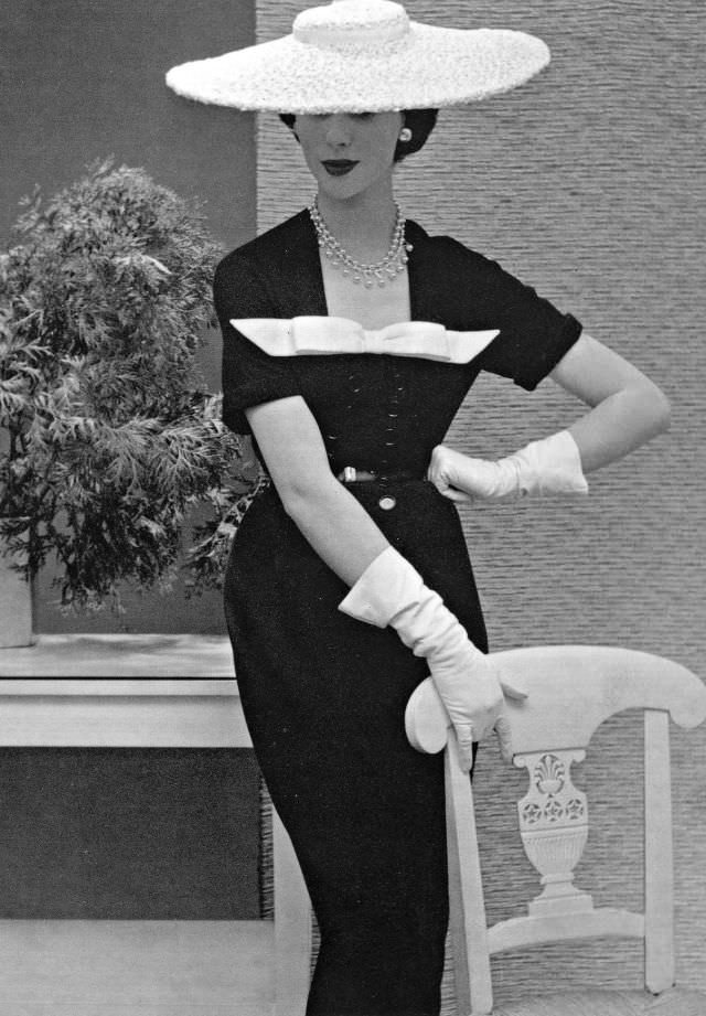 #21 Myrtle Crawford in navy blue dress with white pique bow and white straw hat exemplifies the Nina Ricci style, 1953