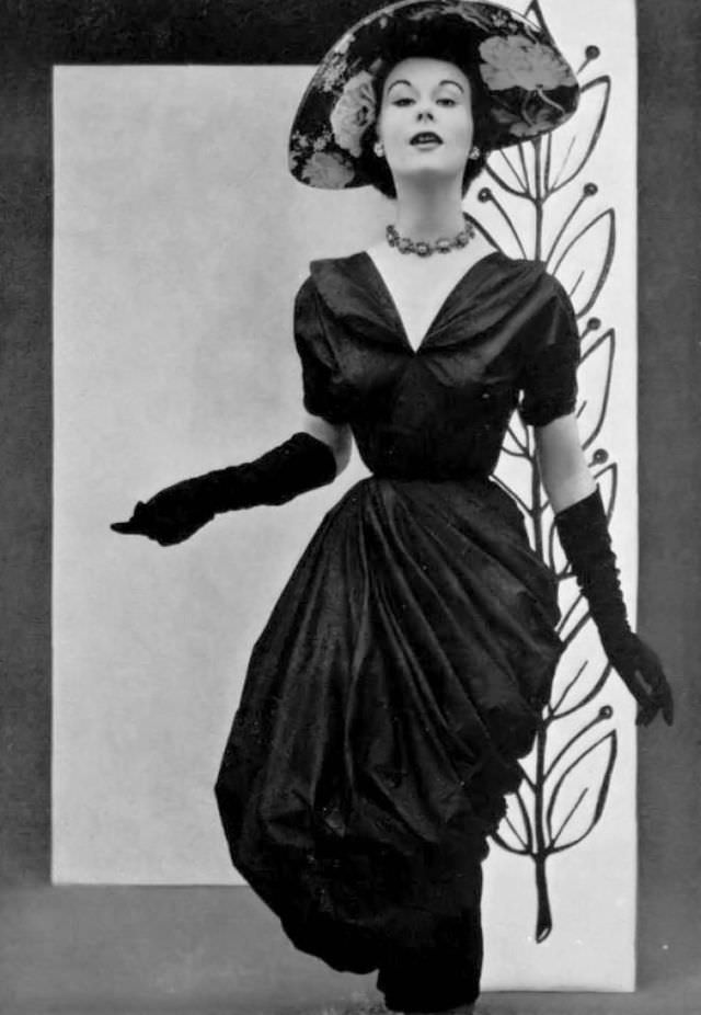 #6 Myrtle Crawford in draped taffeta dress that is rolled up in a style reminiscent of that of a washerwomen’s apron, by Grès, hat by Gilbert Orcel, 1952