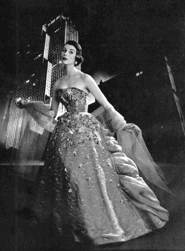 #33 Myrtle Crawford is wearing gala ball gown of dark gray organdy embroidered with frosted multi-colored sequins, worn with light gray tulle stole by Jacques Fath, 1953