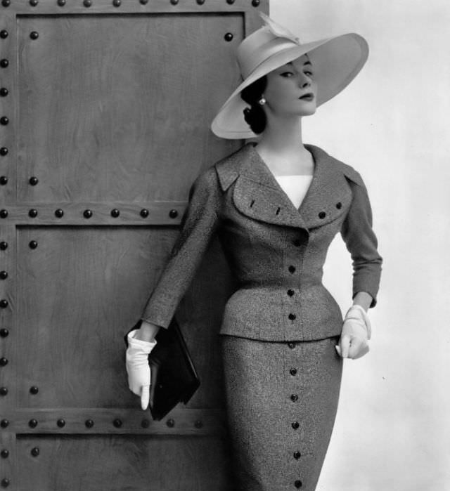 #38 Myrtle Crawford in heather gray wool suit, vertical line continues from the buttoned jacket down the skirt, by Jacques Fath, 1954