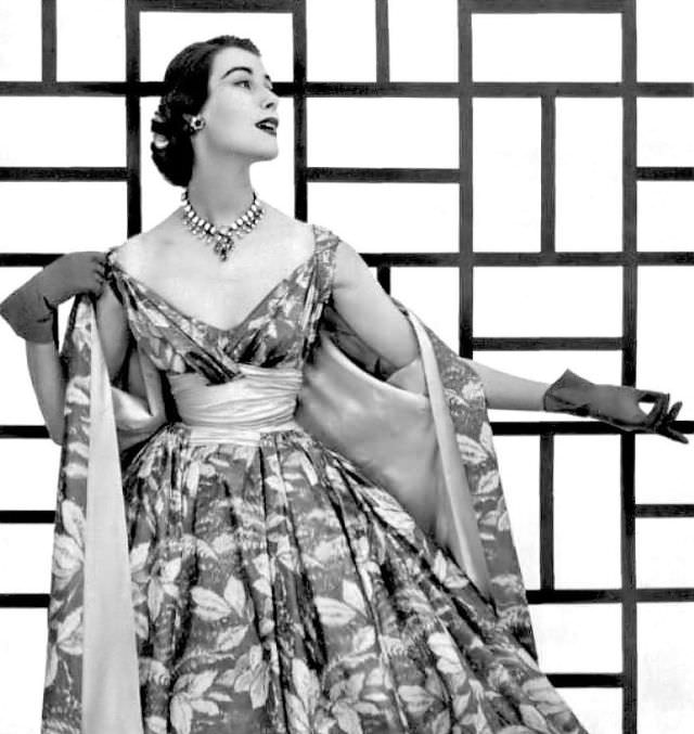 #41 Myrtle Crawford in printed taffeta, high waist in pink taffeta matches the lining of the coat, the short dress has cross-over bodice and wide full skirt, by Pierre Balmain, 1954.