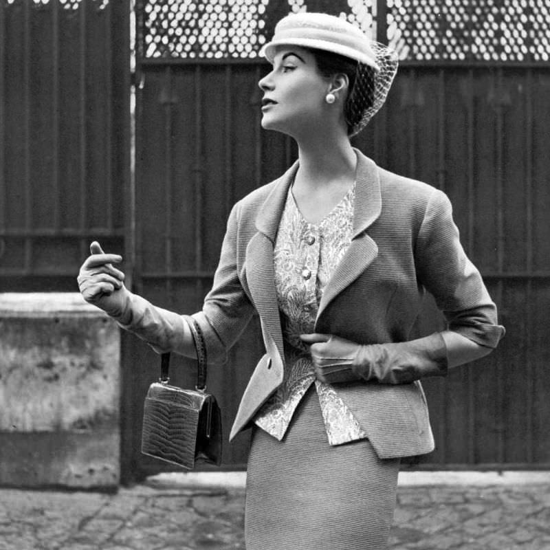 #2 Myrtle Crawford in beige Ottoman suit with fitted jacket indented to v, worn over print cashmere top and narrow skirt by Manguin, hat by Paulette, croc bag by Morabito, 1953