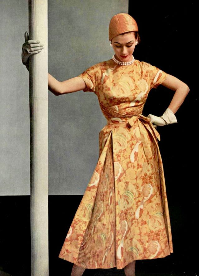 #14 Anne Gunning in silk print dress of various shades of yellow with pleated panels in the skirt and a crossed bodice by Givenchy, 1953