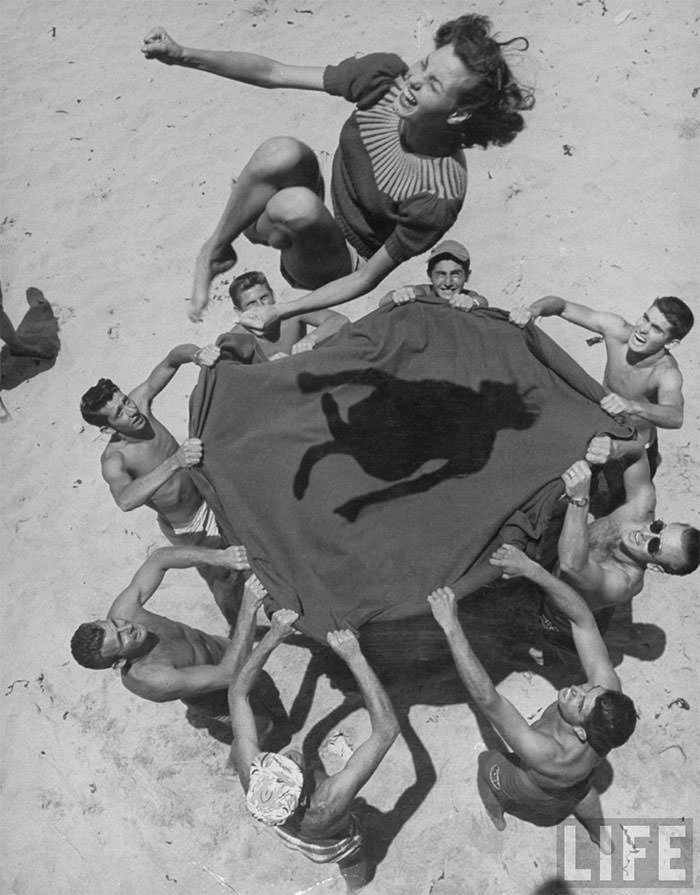 #30 Teenaged boys using blanket to toss their friend, norma baker, into the air on the beach, 1948