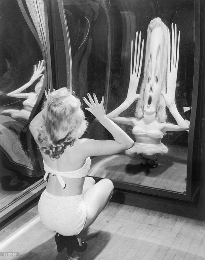#56 A woman in a toweling bikini poses in a funfair hall of mirrors, 1935