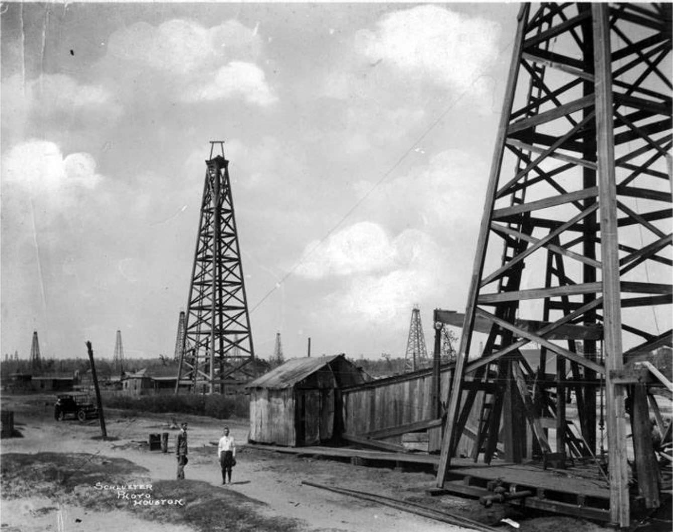 #44 Two men standing on dirt road near an oil well, 1930s.