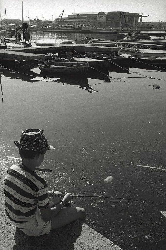 #76 A child fishing in the polluted water of the Viareggio harbour, 1960.