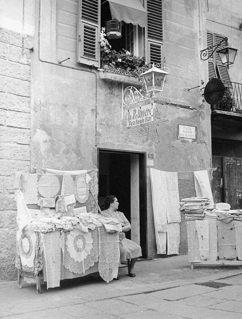 #27 A woman sits at the entrance of the bar La PoliniÃ¨re, next to a stand of laces, 1960s.