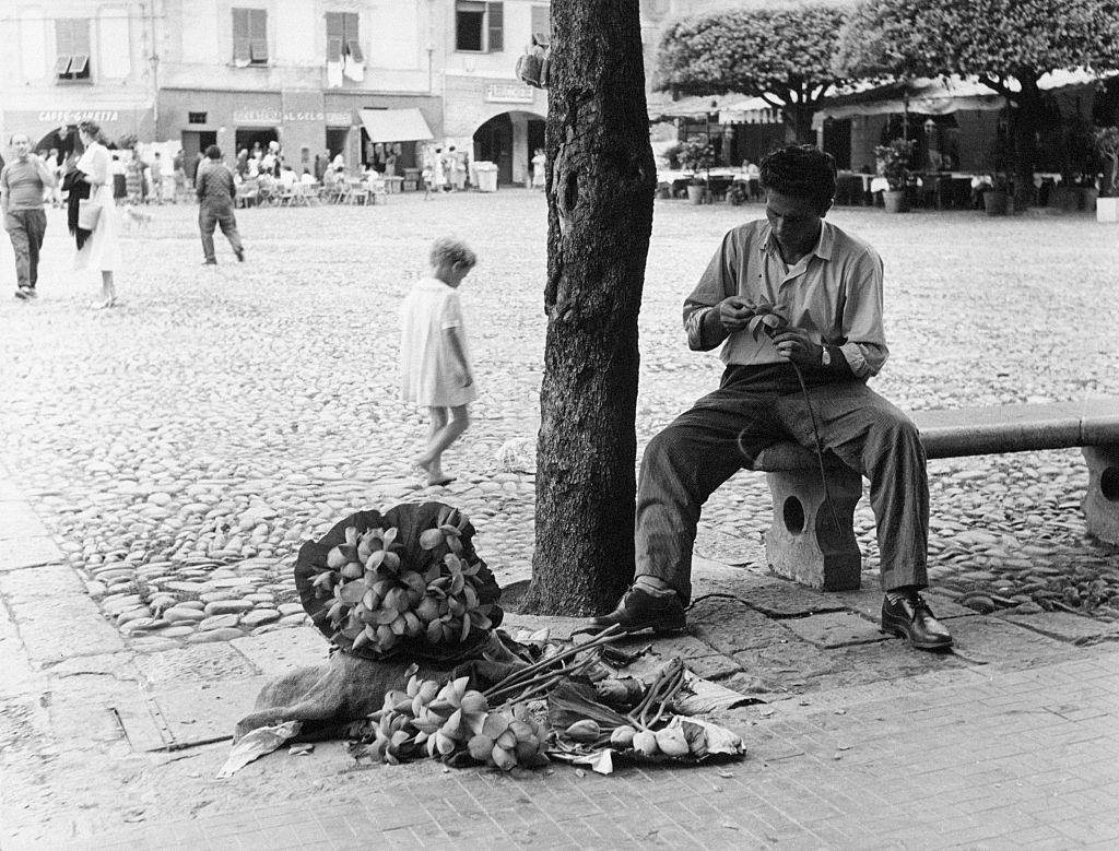 #31 A young man sitting on a bench creates bunches of papier-maché flowers, Portofino, 1960s.