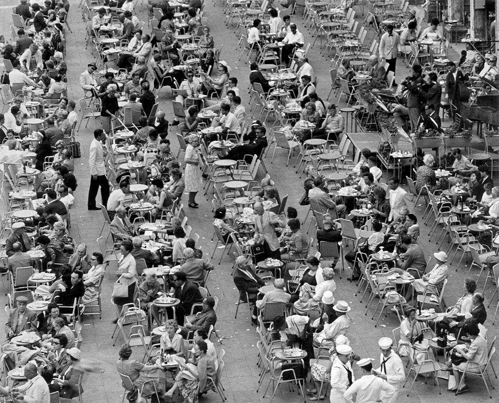 #32 A crowd of people sitting outdoor at the tables of a café. Italy, 1960s