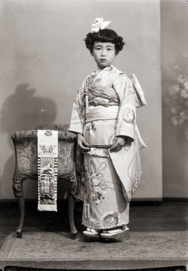 #13 A Japanese girl in a kimono with a bow, geta sandals, and folded fan. She also has the traditional Shichi-Go-San Chitose Ame candy