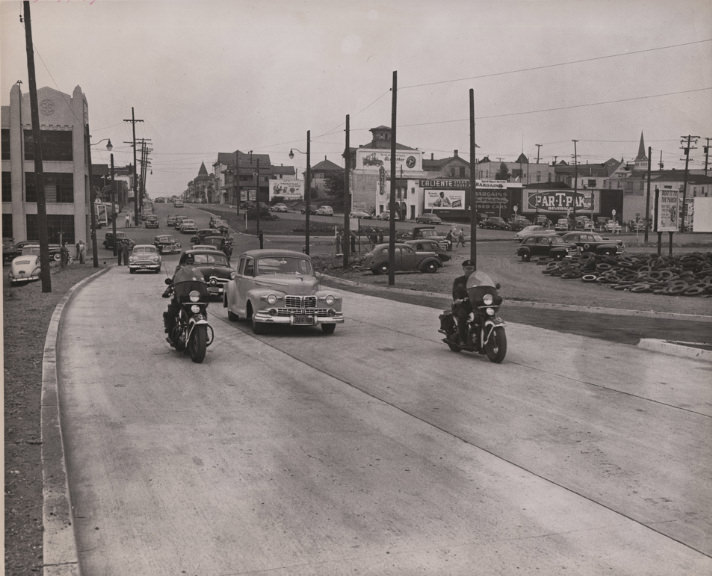 #81 Two policeman on motorcycles escort cars eastbound on East 12th Street, 1940s