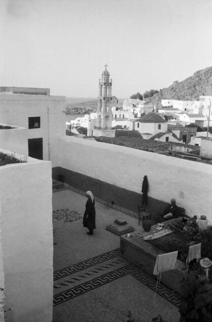 #42 A woman on a roof terrace in the town of Lindos looking towards the Panagia Church on Rhodes, Greece, 1950s.
