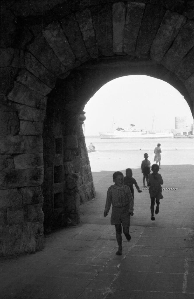 #52 Children run from the harbor through the city walls of Rhodes to play, Greece, 1950s