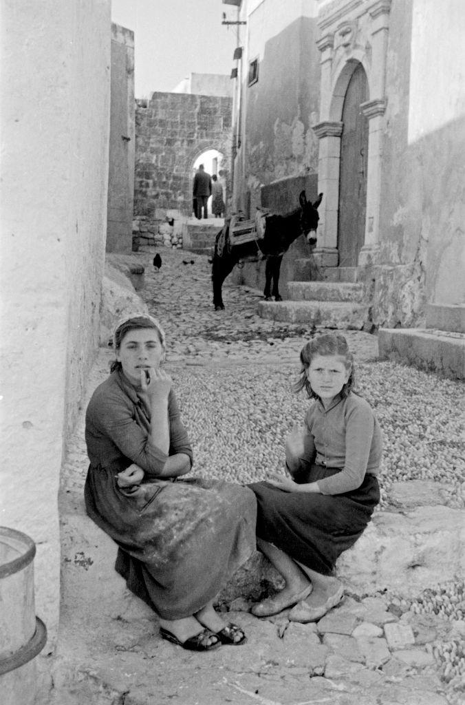 #55 Two young women sit in front of the house on the street having a conversation in Rhodes, Greece, 1950s.