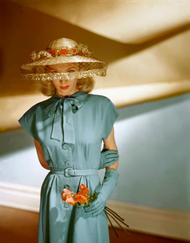 #2 Actress Carole Landis wears a short-sleeved blue dress from a Vogue Pattern together with matching gloves and John Frederics veiled hat, 1945