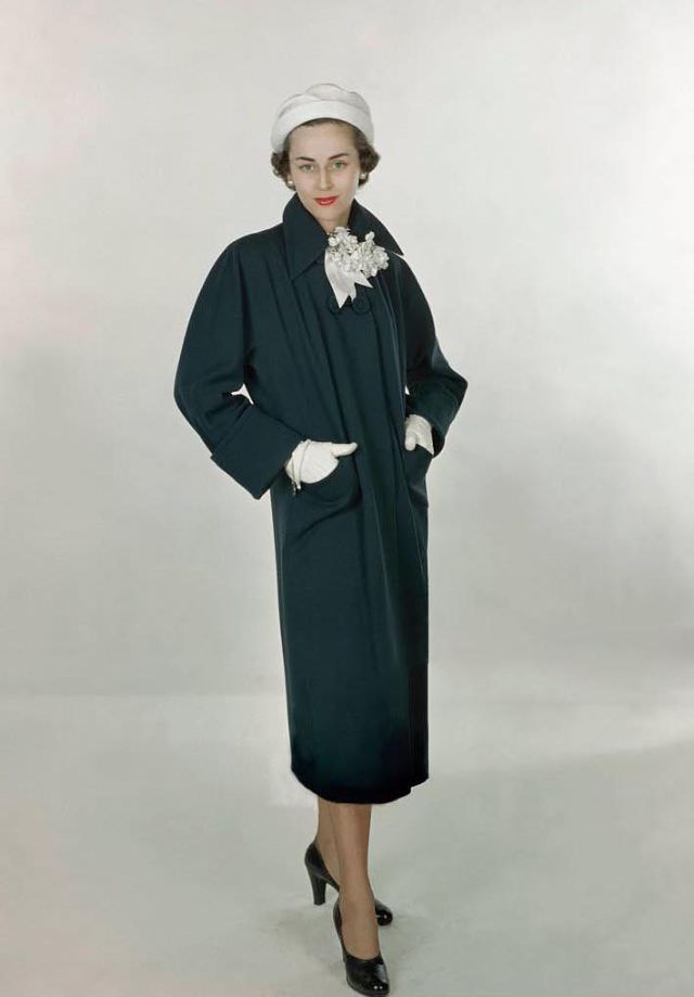#32 Model Joan Petit wearing navy, worsted wool coat by Lassie Maid and Madcaps’ pique hat in white, Glamour, 1948