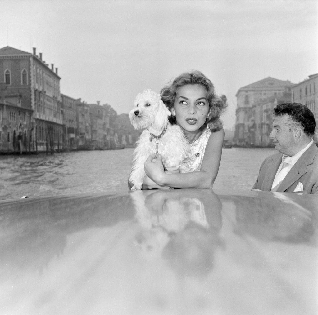 #86 Abbe Lane and actress, enjoys a motorboat ride along the Grand Canal, pictured with her pet dog Suzette, and husband Xavier Cugat.