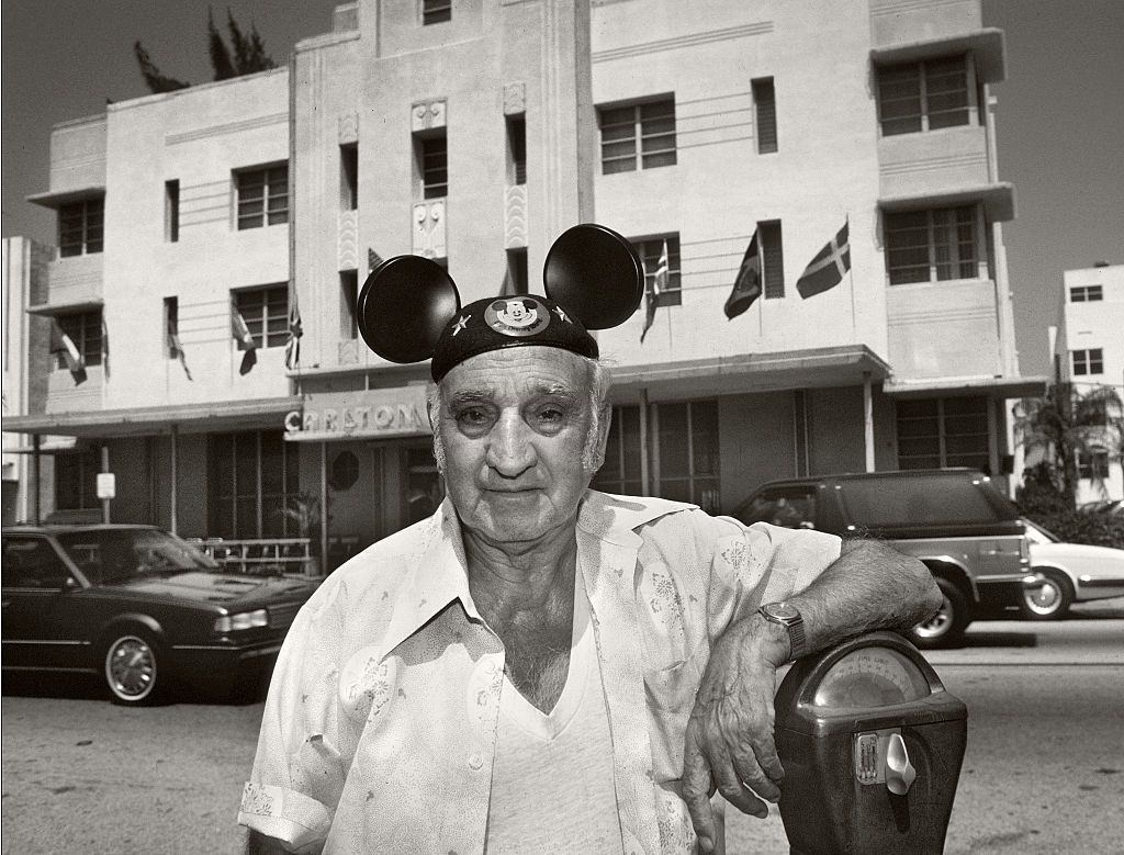 #79 Elderly man standing by a parking meter in front of the Carlton Hotel, Washington Avenue, Miami Beach, wearing a Micky Mouse hat.