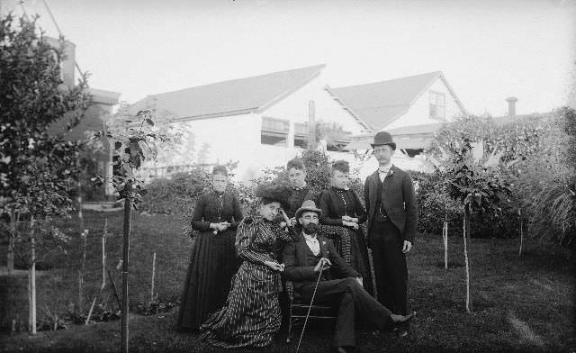 #92 Group of men and women posing for a portrait in the backyard of a house, 1895