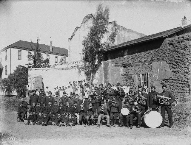 #54 A Native American band standing near the Mission San Diego de Alcala, 1895