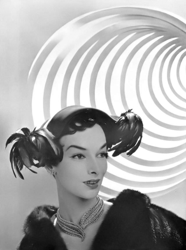 #25 Victoria von Hagen in small velvet cap adorned with rooster tail feathers by Rose Valois, gold necklace by Sterlé, L’Officiel, 1953