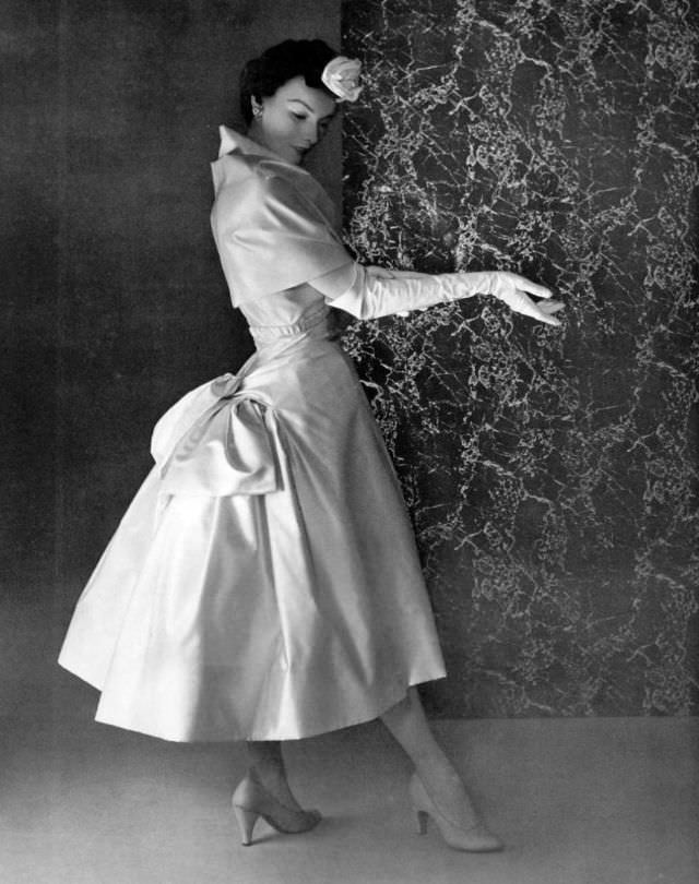 #27 Victoria von Hagen in white satin dinner dress featuring bustle-like bow gathered in the back by Christian, 1953