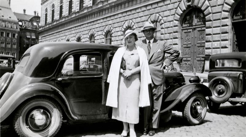 #11 An elegant couple posing with a Citroën 11 CV in front of an impressive Renaissance building in a busy historic town centre, circa 1935