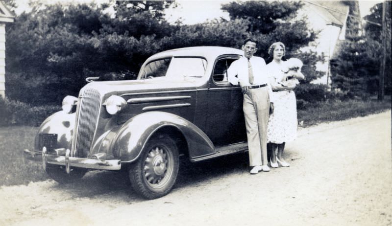 #17 A stylish couple posing with a 1936 Chevrolet Standard Coupe on a gravel road in the countryside on July 22, 1936