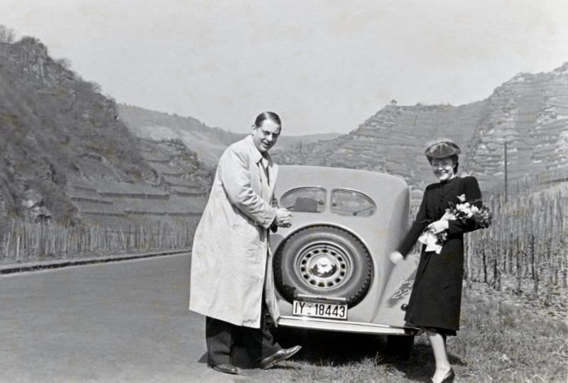 #23 A cheerful couple posing with a Steyr 220 Limousine on a country road in the Ahr Valley, a wine-growing region south of the city of Bonn.