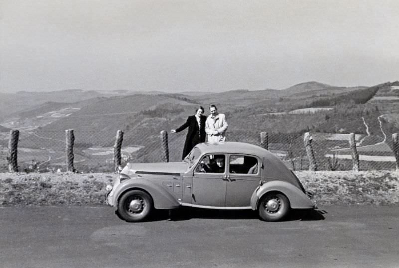 #24 A couple posing with a Steyr 220 Limousine on a mountain road overlooking a valley, 1938