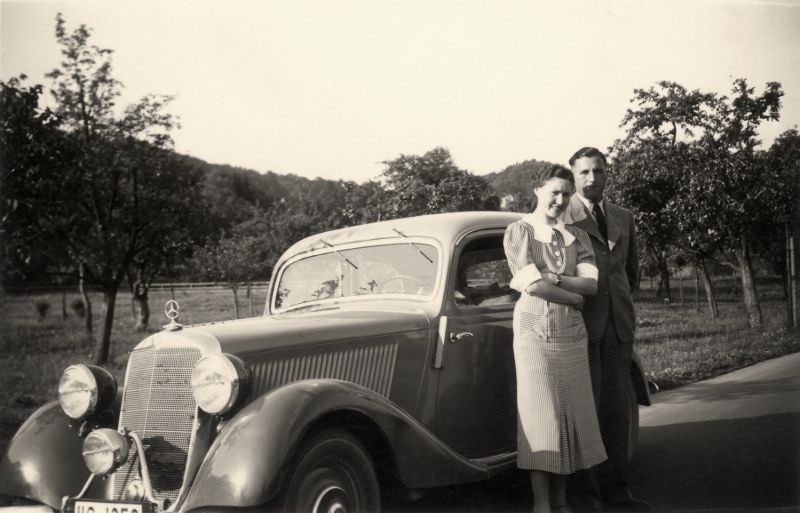 #25 A lady in a short-sleeved dress and a fellow in a suit posing with a Mercedes-Benz 170 V in the countryside.