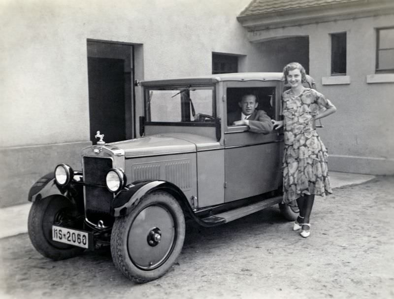 #3 A cheerful lady in a floral dress and a dapper fellow in a suit posing with a Hanomag 4/20 PS Cabriolet-Limousine in the backyard of a private home.