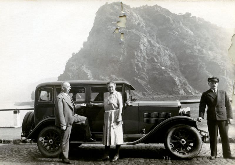 #30 En elderly couple and their chauffeur posing with an 1930 Essex Sedan at Lorelei Rock on the bank of the River Rhine, 1930
