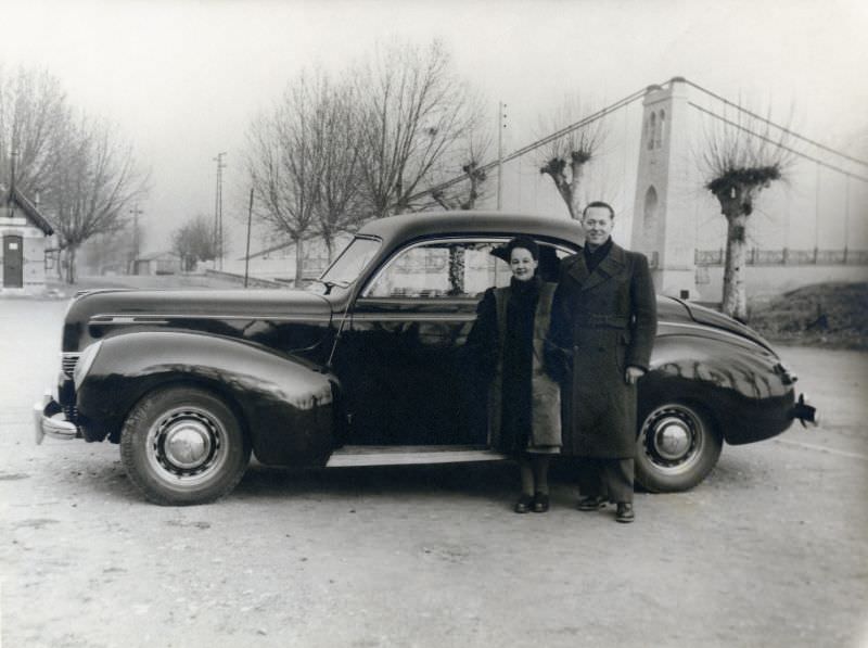 #32 A fashionable couple posing with a 1939 Mercury Eight Club Coupe near a suspension bridge on a bleak winter’s day, 1939