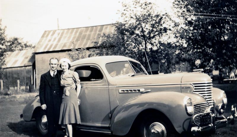 #34 A middle-aged couple posing with a 1939 DeSoto Business Coupe in a back yard in summertime, 1939