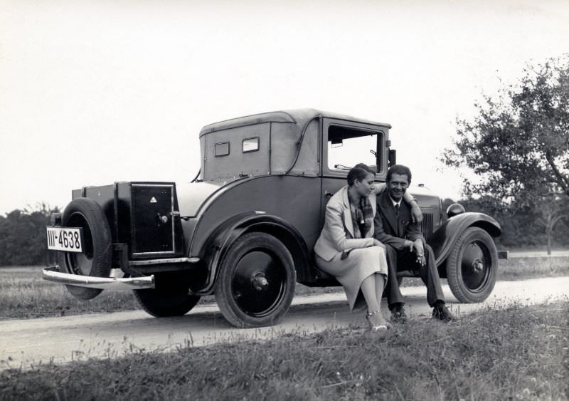 #5 A stylish couple posing on the running board of an Opel 4/20 PS Cabriolet 2 convertible in the countryside.