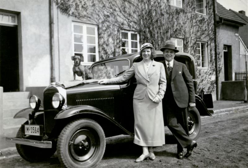 #7 A cheerful couple and posing with an Opel 1,2 Liter in front of a middle-class home in a residential street.