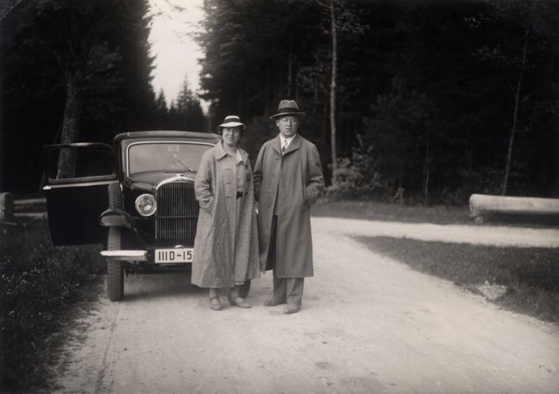 #9 A middle-aged couple wearing raincoats and hats with an Opel 1,2 Liter.
