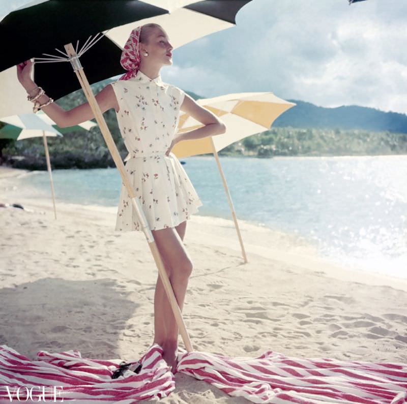 #15 Model standing under beach umbrella wearing summer dress look; pleated short shorts and matching sleeveless shirt, both in a light floral pattern, Vogue, June 1954